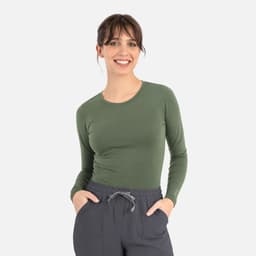 A woman wearing a long-sleeve green underscrub tee paired with grey pants. The tee features a logo.