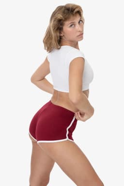 Red interlock running shorts with white piping, featuring a model in a fitted white crop top. Logo present on shorts.