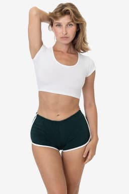 A model poses in green interlock running shorts with white trim, paired with a white cropped top. The shorts have a logo.