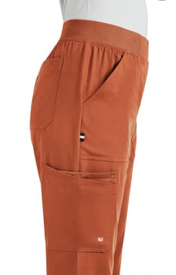 A side view of orange boot cut pants featuring pockets and an elastic waistband. The garment includes a small logo.