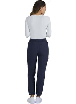 A woman wearing navy Harper Pants, viewed from the back, paired with a white long-sleeve top and slippers.