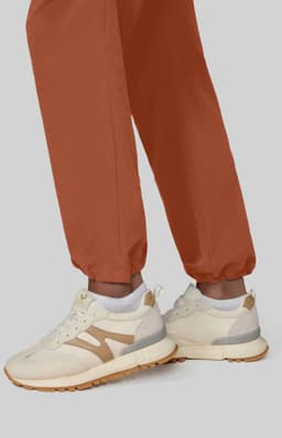 Wide leg pants in a rich terracotta hue, paired with cream and beige sneakers, displayed against a neutral background.