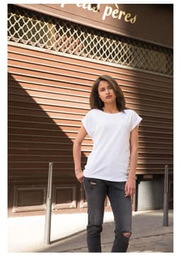 A model wearing a white casual T-shirt paired with distressed black jeans, standing in an urban setting.