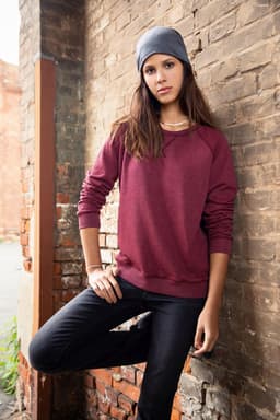 A maroon jumper with long sleeves worn by a model, paired with a grey beanie, set against a brick wall.