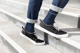 A pair of navy organic socks worn with black shoes, standing on outdoor steps with rolled-up denim jeans.