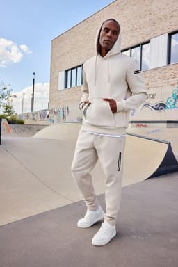 A men's interlock hoodie in beige, paired with matching pants, features a logo and a relaxed fit.