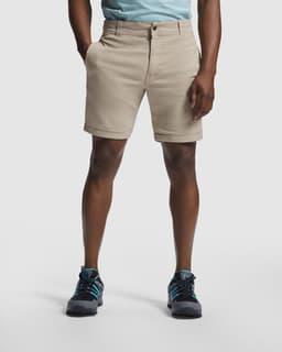 Beige dress shorts displayed on a model, featuring a logo on the waistband and styled with outdoor footwear.