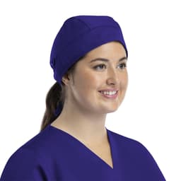 A unisex scrub cap in purple with buttons, worn by a smiling woman in a scrub top.