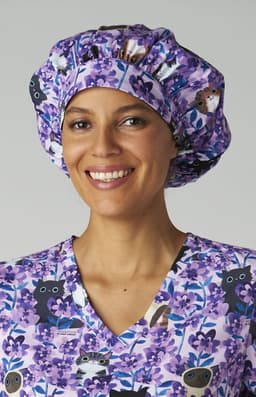 A bouffant cap featuring a purple floral print, worn by a smiling woman in a matching scrub top.