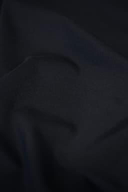 A close-up of a textured black fabric, showcasing its smooth and soft material. The image features subtle folds and shadows.