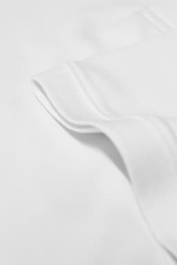 A close-up of a white polo shirt, featuring the fabric texture and a folded collar. The shirt has a logo.
