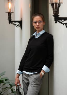 A black knitwear jumper paired with a light blue shirt and styled with grey trousers, featuring a logo.