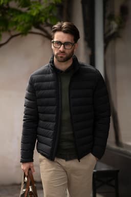A man wearing a black puffer jacket with a fitted design, carrying a brown bag, standing outdoors.