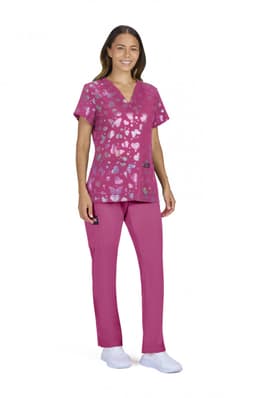 A woman wearing a pink scrub top with a heart pattern and matching scrub pants. The outfit includes a pocket detail.