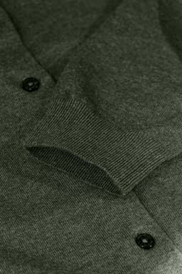 A green cardigan featuring a knit texture and button details, highlighting the sleeve and cuff.