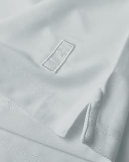A white polo shirt featuring a hem split and a logo. The fabric has a textured appearance.