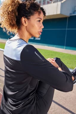A long-sleeve ladies' running shirt in black and grey, featuring a logo, displayed on a model outdoors.