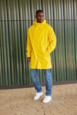 A unisex yellow raincoat features a hood and is styled over blue jeans and white sneakers. It has a logo.