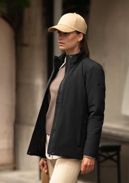 A woman wearing a black jacket with a beige cap, standing against a neutral background.