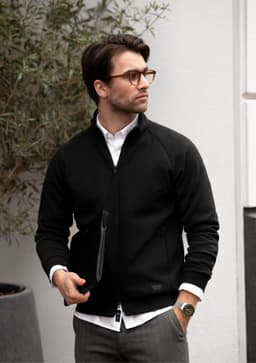 A black Eaton Men Jacket with a zip front, worn by a man in glasses, against a neutral backdrop.