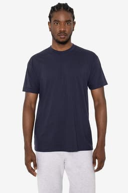 A man models a navy blue short sleeve cotton poly crew tee with a logo, paired with grey sweatpants.