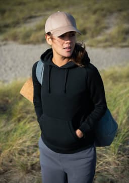 A black hoodie worn by a woman, paired with a cap, standing outdoors with grass in the background.