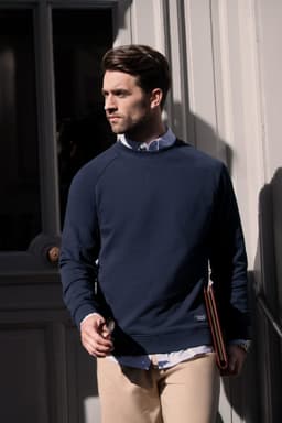 A navy sweatshirt worn by a man, with a logo visible. He is standing by a door, holding a folder.