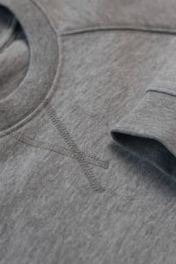 A grey sweatshirt featuring a crew neck and long sleeves, with a subtle logo and stitching detail.