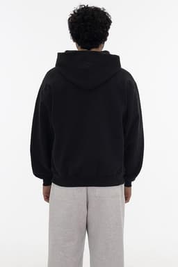 A black heavy fleece zip-up hoodie displayed on a model from the back, paired with grey sweatpants.