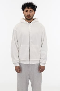 A heavy fleece zip-up hoodie in cream, featuring a hood and a front zipper. The model wears grey pants.