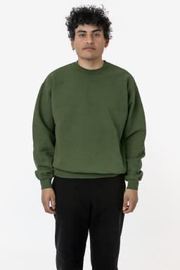 A green heavy fleece pullover is worn by a model standing in a neutral setting, with a logo visible on the garment.