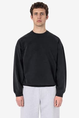 A black garment dye heavy fleece pullover worn by a model, styled with grey trousers. It features a logo.