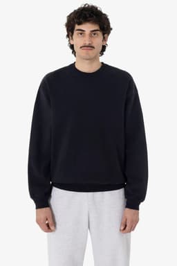 A man wearing a black garment dye heavy fleece pullover, paired with light grey sweatpants. The pullover features a logo.