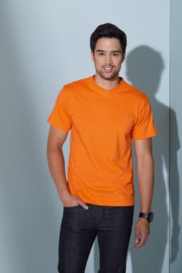 An orange V-T Medium T-shirt worn by a smiling man, standing against a pale blue wall.