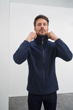 A navy full-zip fleece jacket on a man, featuring a high collar and zipped front. The jacket has a brand logo.
