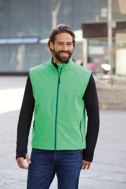 A green softshell vest with a zip front, paired with a black long-sleeve top, worn by a smiling man outdoors.