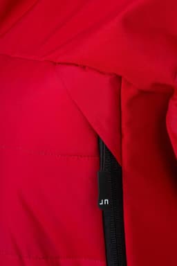 A close-up of a red men's outdoor hybrid jacket, highlighting the soft shell fabric and zipper. It features a logo tag.