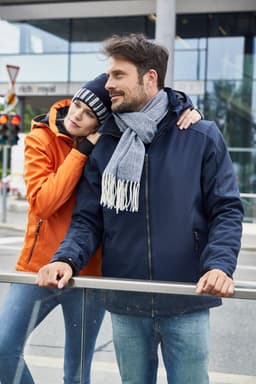 A navy soft shell jacket with a grey scarf is worn by a man, while a woman in an orange jacket leans against him.