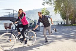 A pink ladies down vest is worn by a woman cycling, while a man runs alongside in a black vest.