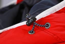 A close-up of a red vest featuring a black toggle and blue decorative cord detail.