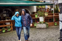 A blue ladies rain jacket with a hood, worn by a woman, alongside a man in a navy jacket, outdoors in a market setting.