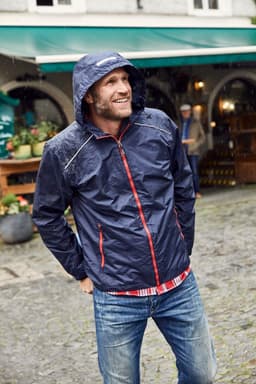 A navy blue men's rain jacket with red accents and a hood, worn by a smiling man outdoors.
