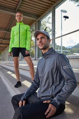 A grey men's softshell jacket with a logo, paired with a model in a bright green jacket, both in an outdoor setting.