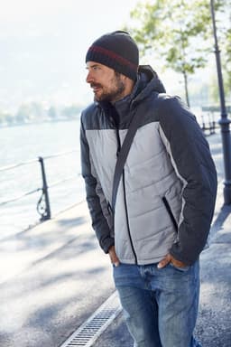 A men's puffer jacket in grey and dark grey, featuring a hood, with a casual beanie and denim jeans.