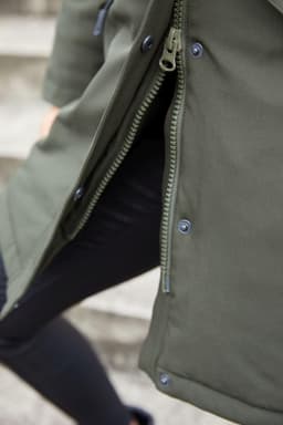 A close-up of a dark green ladies' business parka featuring a zipper and snap buttons. The fabric appears water-resistant.