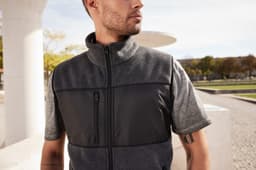 A men's fleece vest in grey with a black panel, featuring a zip front and a high collar.