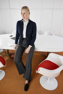 A navy ladies zip-cardigan displayed on a model, paired with grey trousers, in a modern office setting.
