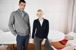 A grey men's zip cardigan and a navy women's zip cardigan, both styled in a modern meeting space.