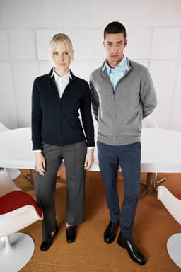 A navy ladies zip-cardigan and a grey men's zip-cardigan, both featuring a logo, styled in a modern office setting.