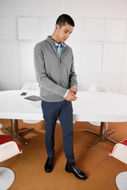 A grey zip cardigan worn over a blue shirt, paired with navy pants and black shoes, set in a modern office environment.
